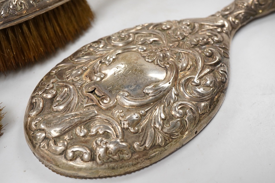 A late Victorian embossed silver four piece dressing table mirror and brush set, by William Comyns, London, 1891/5 and a similar clothes brush.
